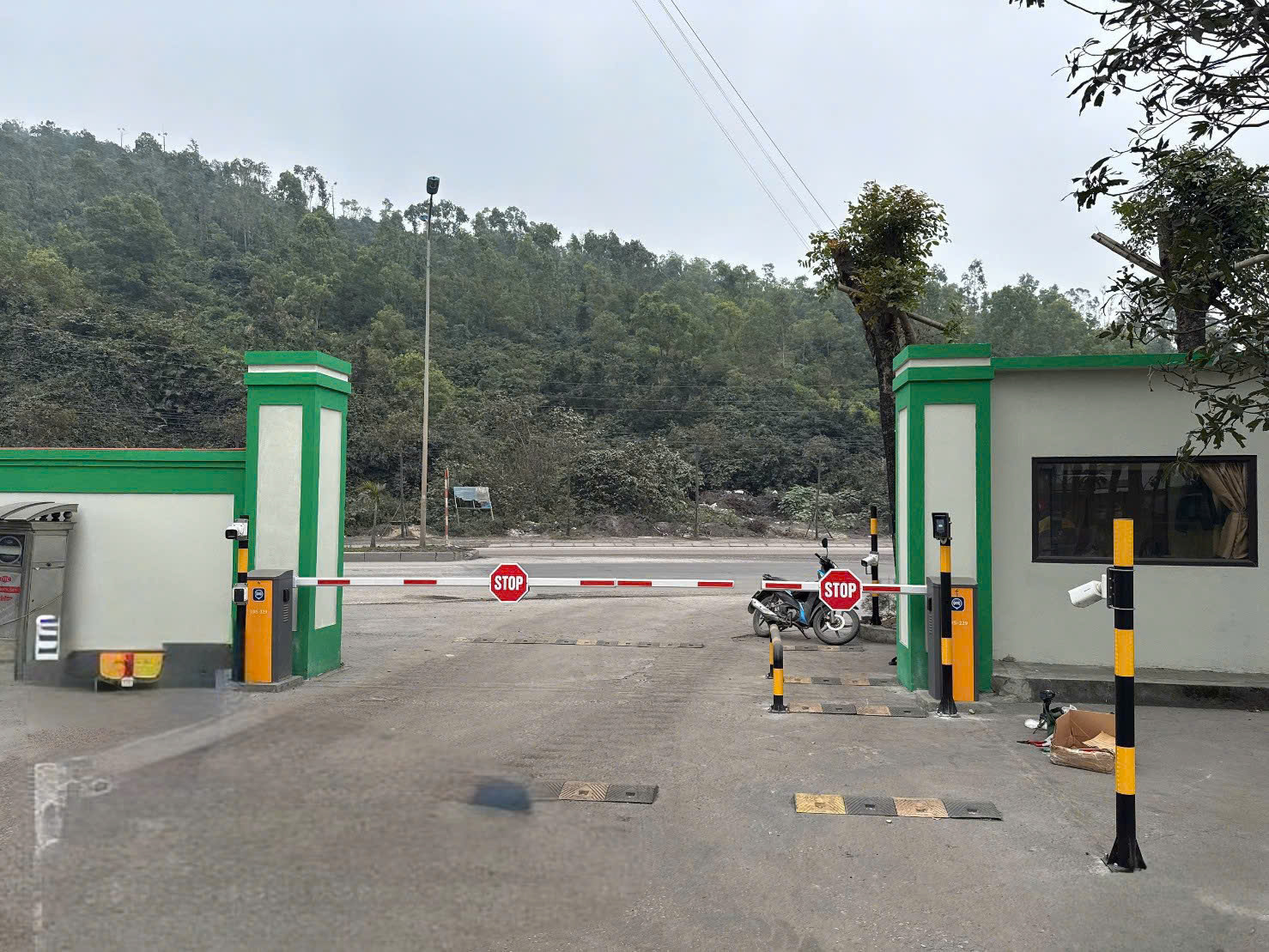 Cổng kiểm soát ra vào tự động với barie, biển báo dừng và camera giám sát trước khu rừng
